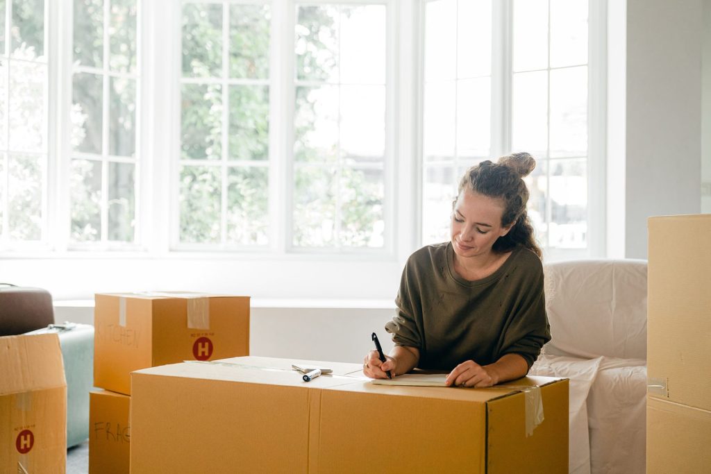 Jeune femme qui écrit sur des cartons de démenagement 